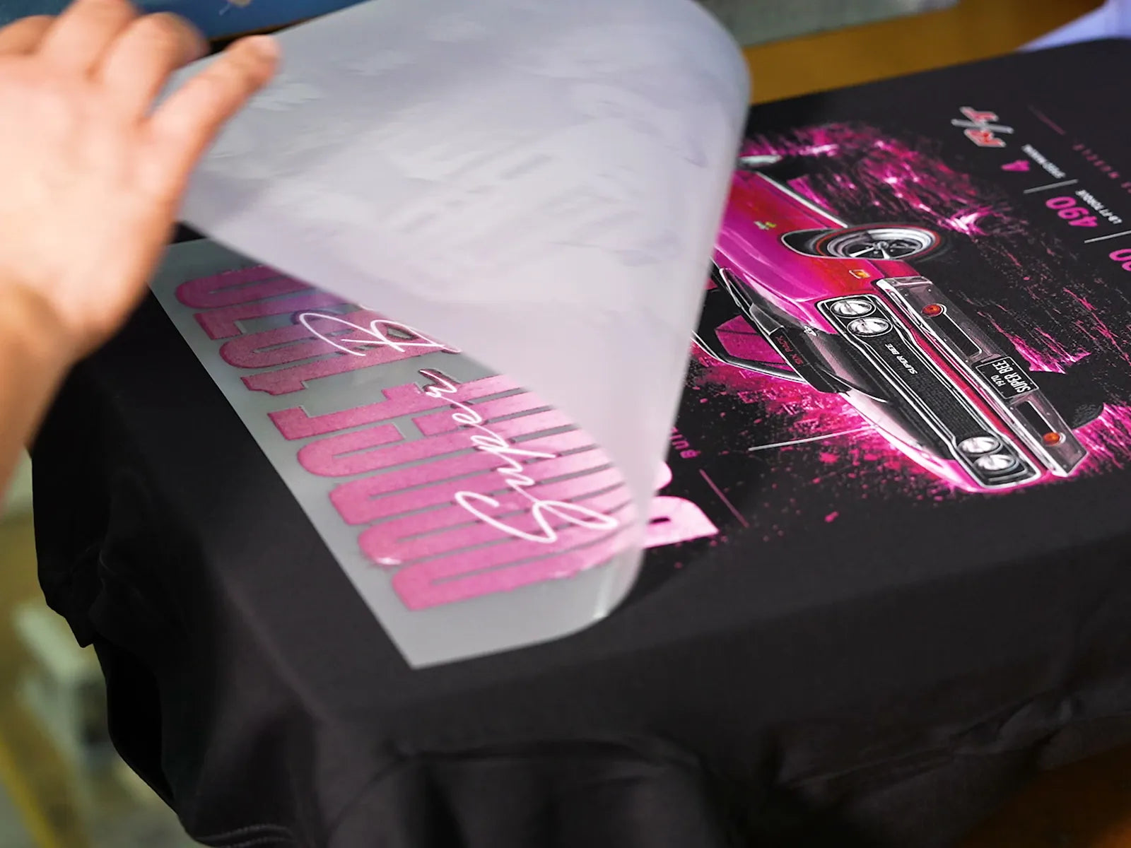 Peeling the carrier away to reveal a pink car print pressed onto a black T-shirt